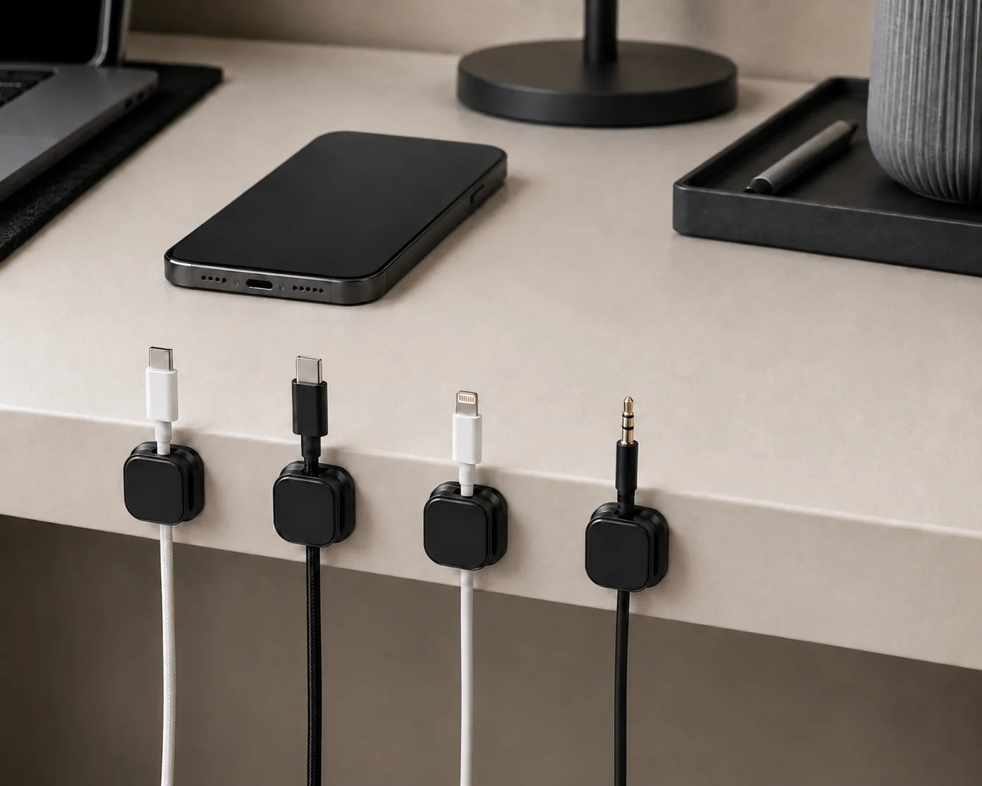 CableRest, Anwendungsszene, schwarzer Kunststoff, vier Kabelhalter mit verschiedenen Kabelenden an heller Schreibtischkante